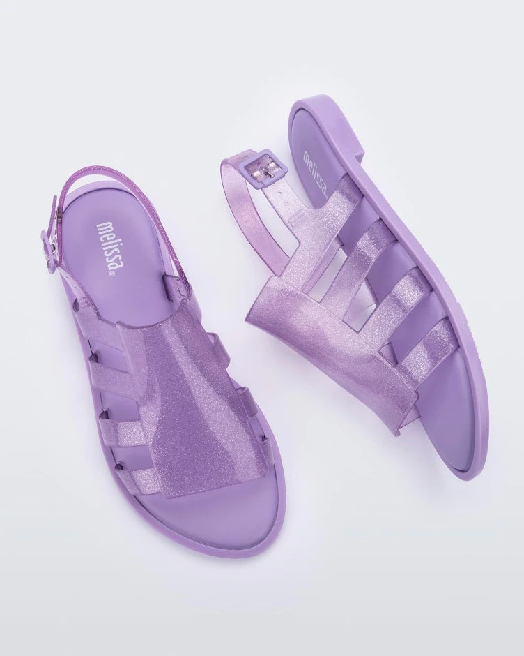 A top and side view of a pair of transparent lilac glitter Melissa Boemia sandals with straps conjoining in the front and a back buckle.
