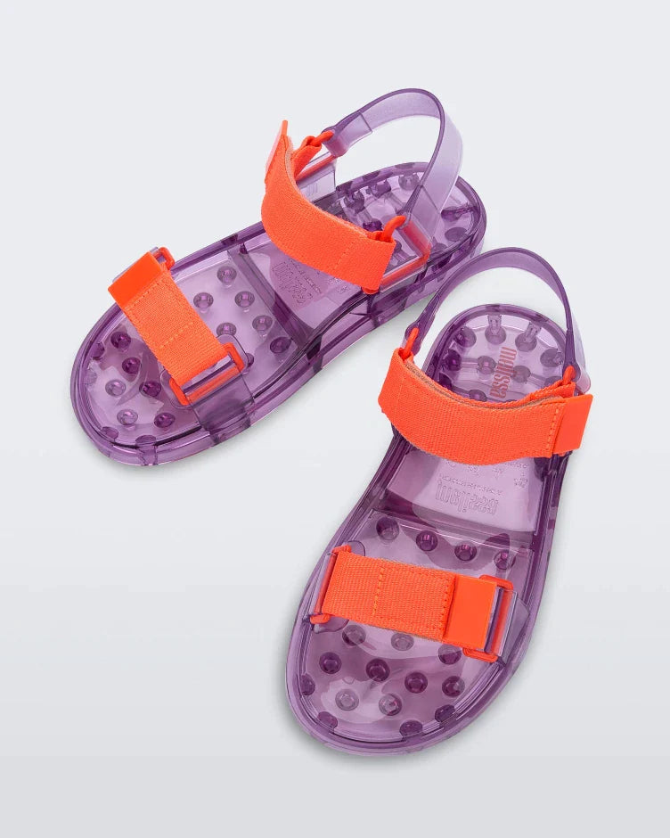Top view of a pair of Melissa Wide Papete sandals with transparent Purple sole and orange velcro straps. 