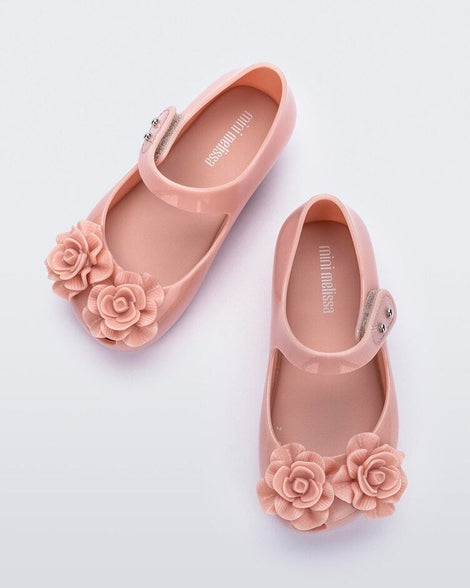 Top view of a pair of light pink Mini Melissa Ultragirl Garden flats with a top strap and two rose details on the toe.