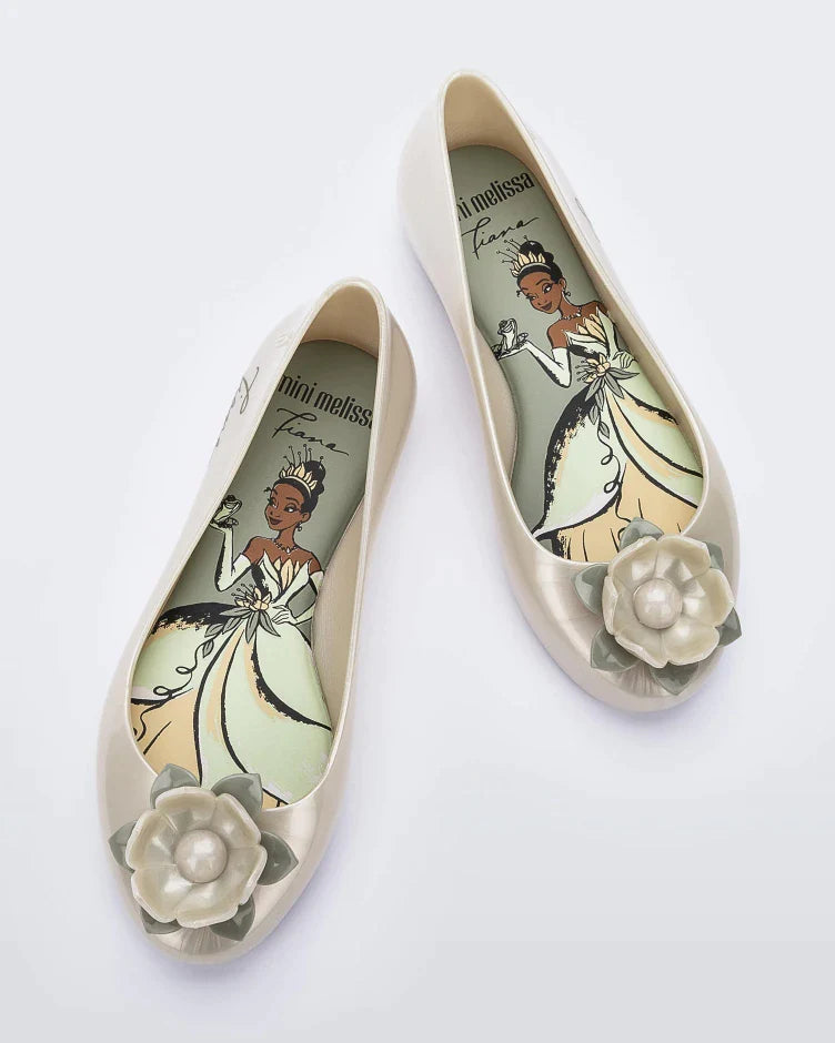 Top view of a pair of green Mini Melissa Sweet Love Princess flats, with a pearly green base, Tiana in script on the side, a flower detail on the toe, and a drawing of Tiana of The Princess and the Frog on the sole.