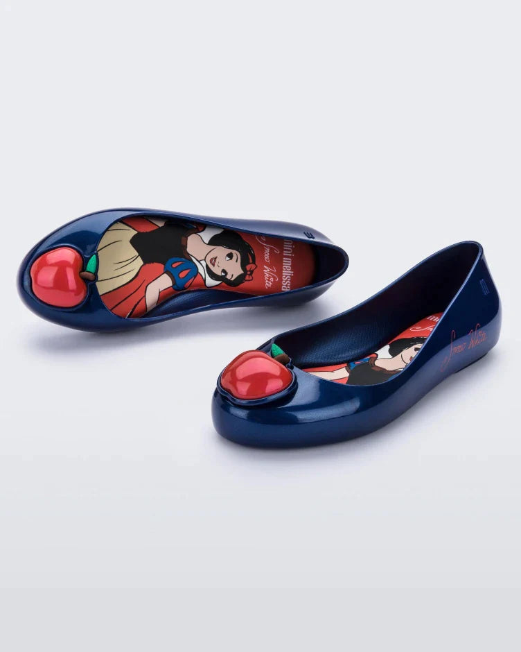 A front and top view of a pair of blue Mini Melissa Sweet Love Princess flats, with a blue base, Snow White in script on the side, an apple detail on the toe, and a drawing of Snow White on the sole.