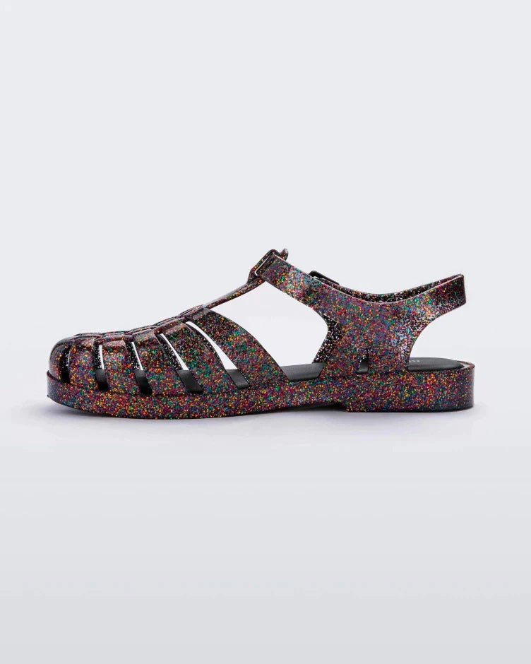 Inner side view of a multicolored glitter Melissa Possession sandal with a closed toe front weft design connected to a top strap with a buckle.