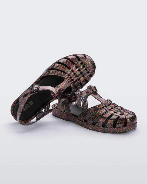 Top and side view of a pair of multicolored glitter Melissa Possession sandals with a closed toe front weft design connected to a top strap with a buckle.