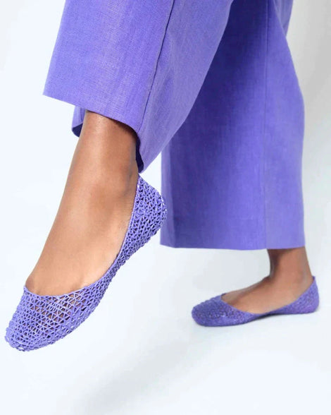 A close up of a person wearing a pair of Melissa Campana purple flats with matching purple pants.