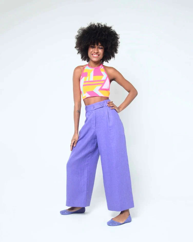 A woman posing wearing a pair of purple Melissa Campana flats with open woven texture worn with a pair of cropped purple pants and a patterned tank top.