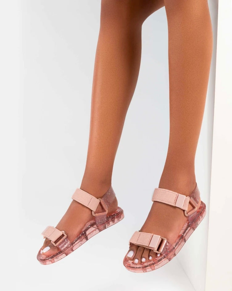 Model's legs wearing a pair of Melissa Wide Papete sandal with transparent pink glitter sole with pink velcro straps 