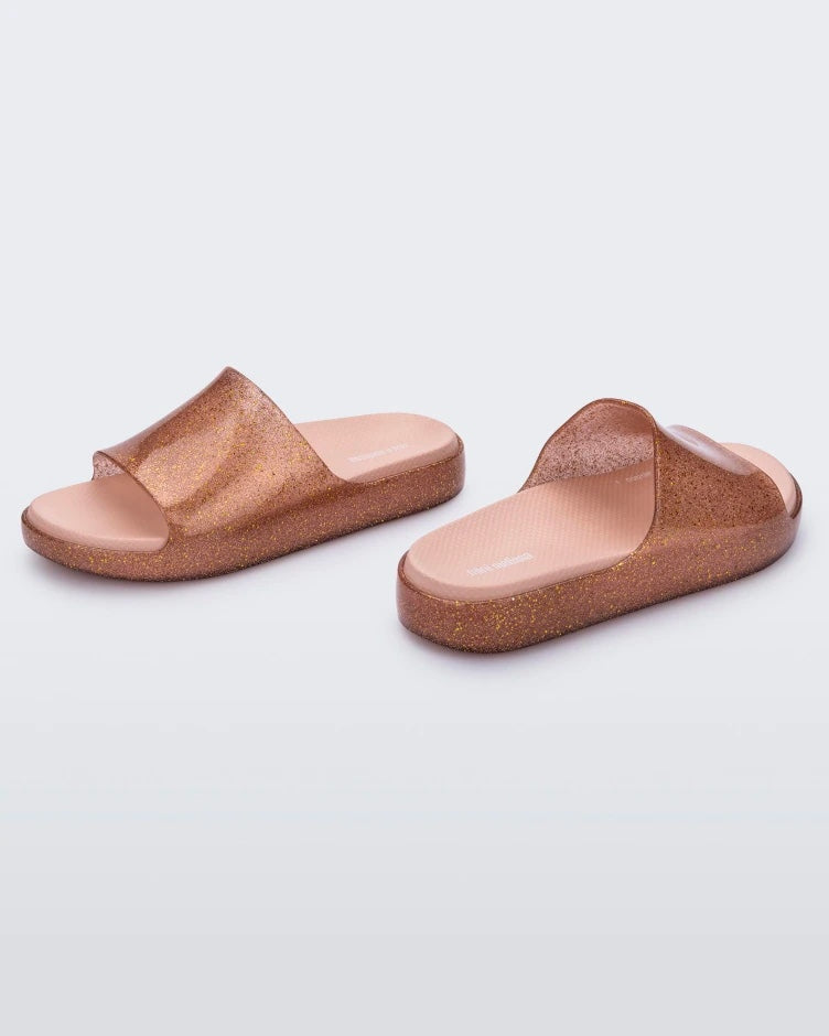 An angled side view of a pair of glitter pink Mini Melissa Cloud slides.