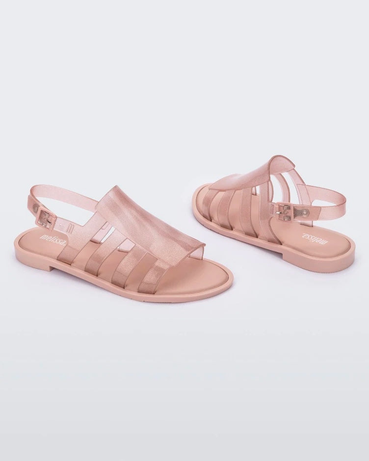 An angled side and back view of a pair of transparent glitter pink Melissa Boemia sandals with straps conjoining in the front and a back buckle.