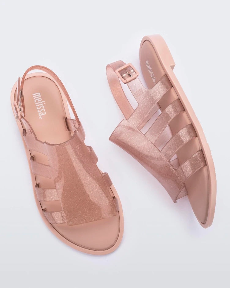 Top and side view of a pair of transparent beige glitter Melissa Boemia sandals with straps conjoining in the front and a back buckle.