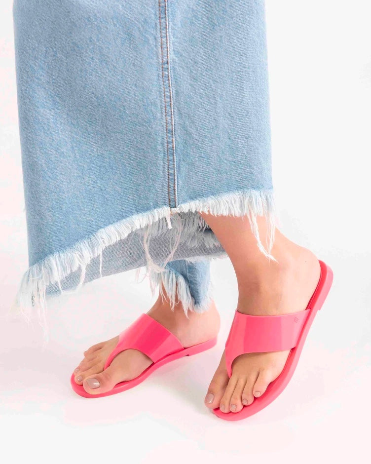 A model's legs wearing a pair of pink Melissa's Essential Chic Flip Flops with a wide upper strap.