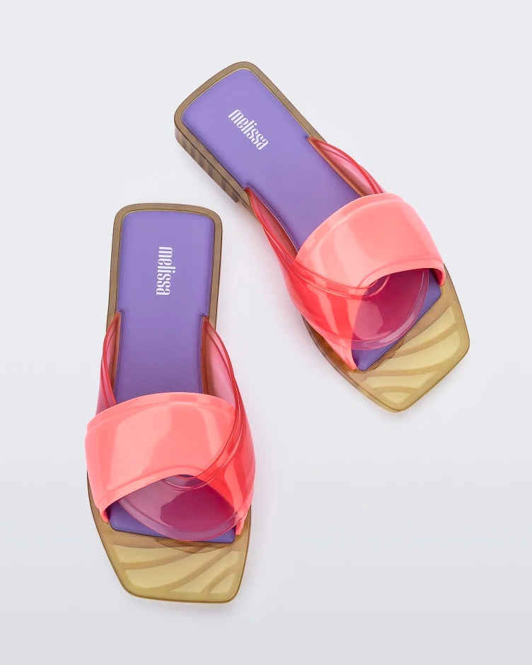 A top view of a pair of pink/green/lilac Melissa Brigitte slides with a pink weft designed upper strap and purple and green insole.