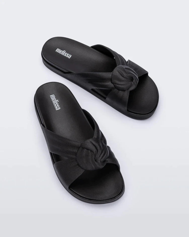 Top view of a pair of black Melissa Plush slides with a twist front detail.