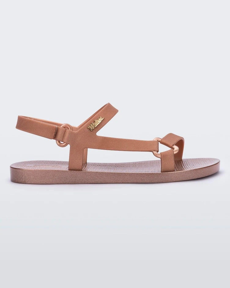 Side view of a rose metallic Melissa Sun Downtown sandal with a front and ankle strap joined together by a vertical strap and a triangle buckle.
