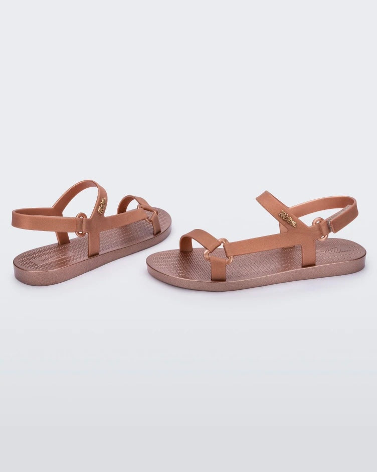 Side and back view of a pair rose metallic Melissa Sun Downtown sandals with a front and ankle strap joined together by a vertical strap and a triangle buckle.