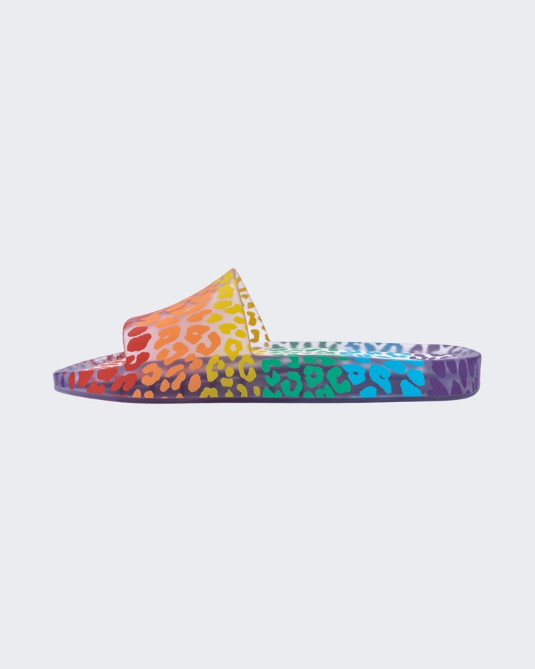 An inner side view of a clear / orange Melissa Rainbow Beach slide with a clear base and a rainbow cheetah print pattern.