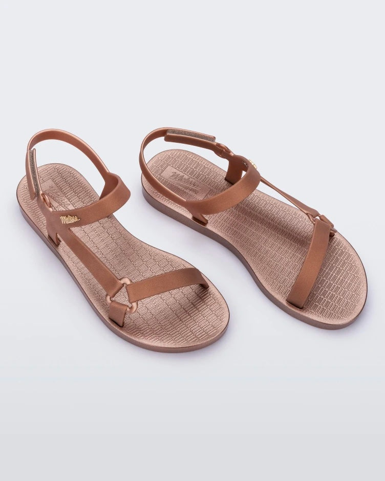 An angled top view of a pair rose metallic Melissa Sun Downtown sandals with a front and ankle strap joined together by a vertical strap and a triangle buckle.
