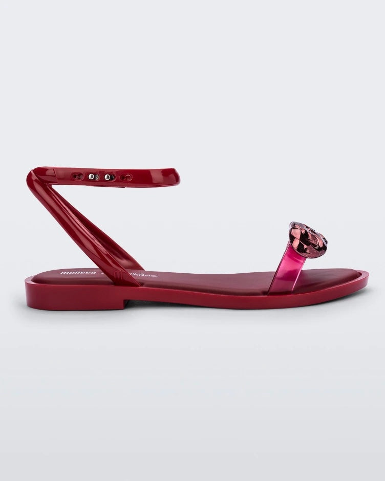 Side view of a red Melissa Dare sandal with a red metal chain buckle.