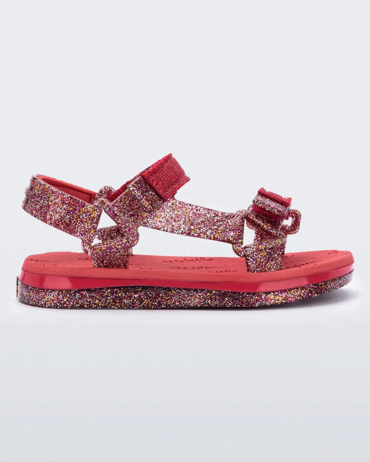 Side view of a red and glitter Mini Melissa Papete sandal.