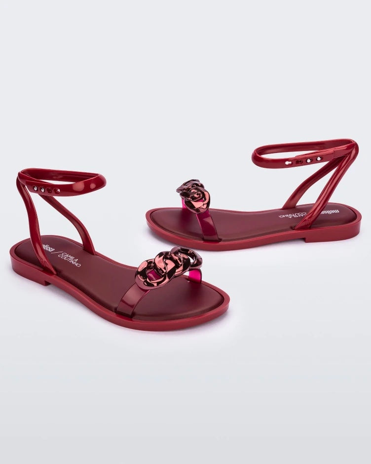Side view of a pair of red Melissa Dare sandals with a red metal chain buckle.