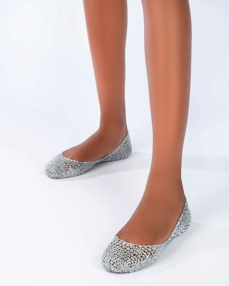 A model's legs wearing a pair of silver glitter Melissa Campana ballet flats.