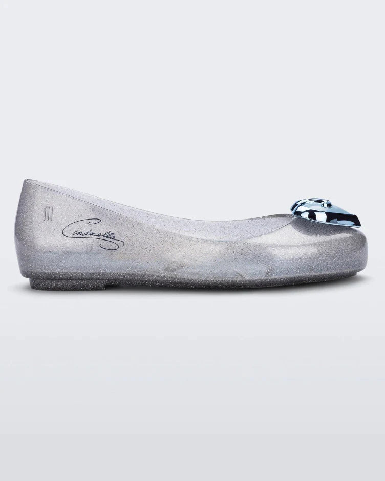 Side view of a silver Mini Melissa Sweet Love Princess flat, with a silver base, Cinderella in script on the side, a heart detail on the toe, and a drawing of Cinderella on the sole.