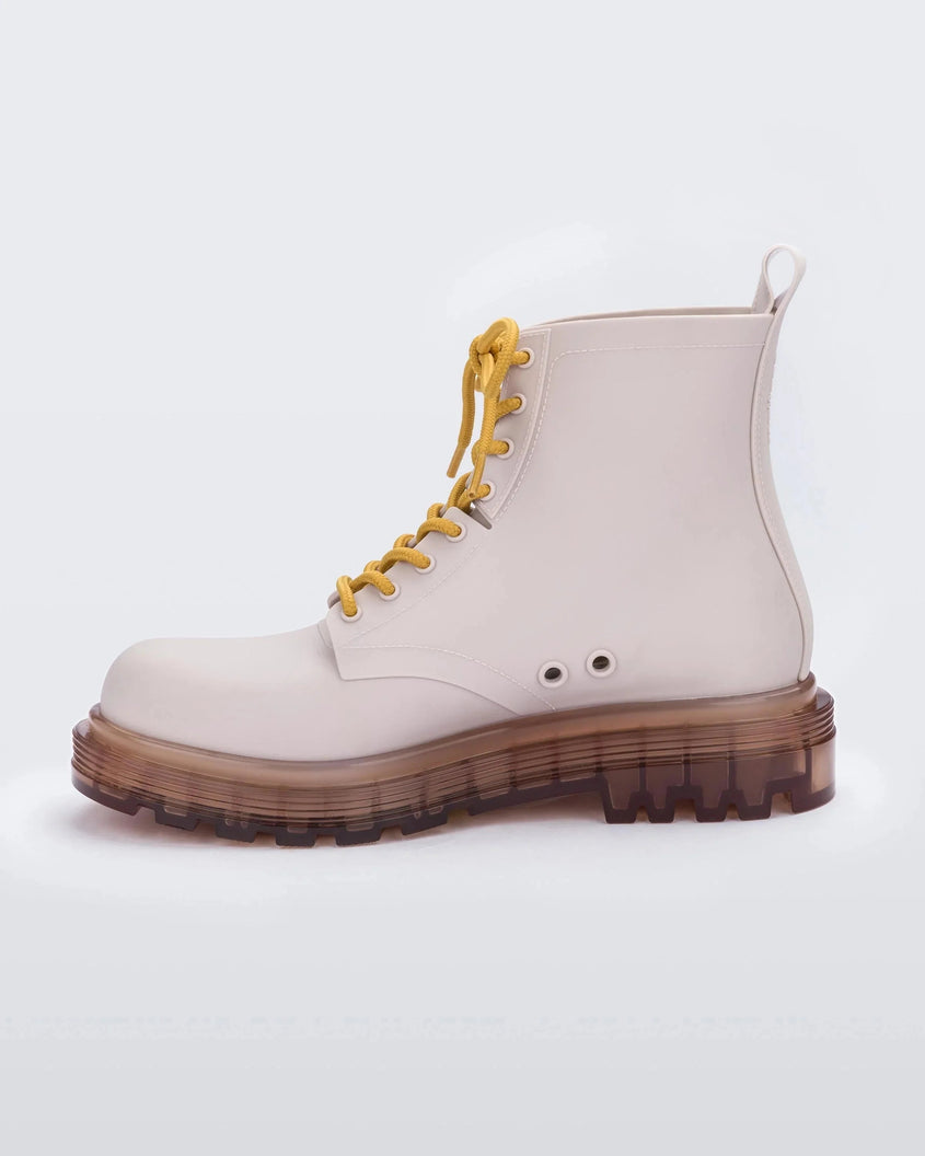 An inner side view of a matte beige/yellow Melissa Coturno boots with a matte beige base, yellow laces and a brown sole. 