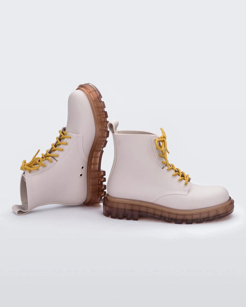Side view of a pair of matte beige/yellow Melissa Coturno boots, one upright and one on it's side, with a matte beige base, yellow laces and a brown sole. 