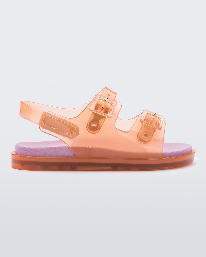 An outter side view of a Orange/Pink Mini Melissa Wide Sandal with a clear orange base, two buckles at the top, a velcro ankle strap and a pink insole.