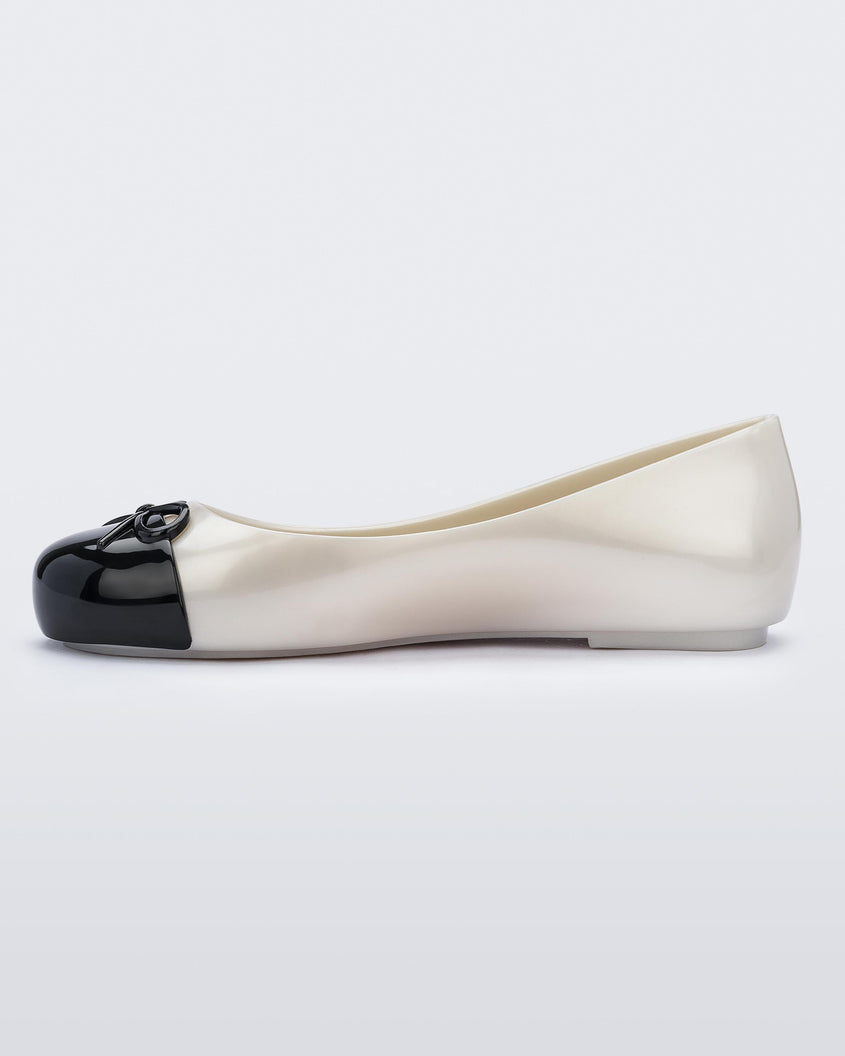 An inner side view of a white Mini Melissa Sweet Love Cap Toe flat with a white base and a black toe cap with a bow on top.