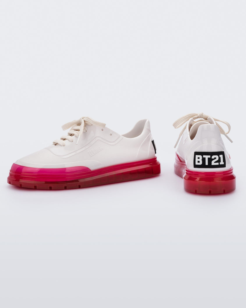 A side and back view of a pair of white Melissa Classic sneakers with a white base, laces, pink sole and a melissa logo on the side.