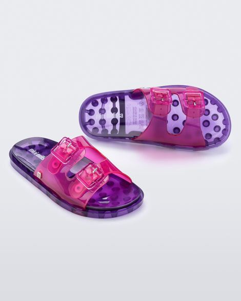 An angled front and top view of a pair of pink/lilac Mini Melissa Wide Slides with a pink top with two pink buckles and a lilac sole.