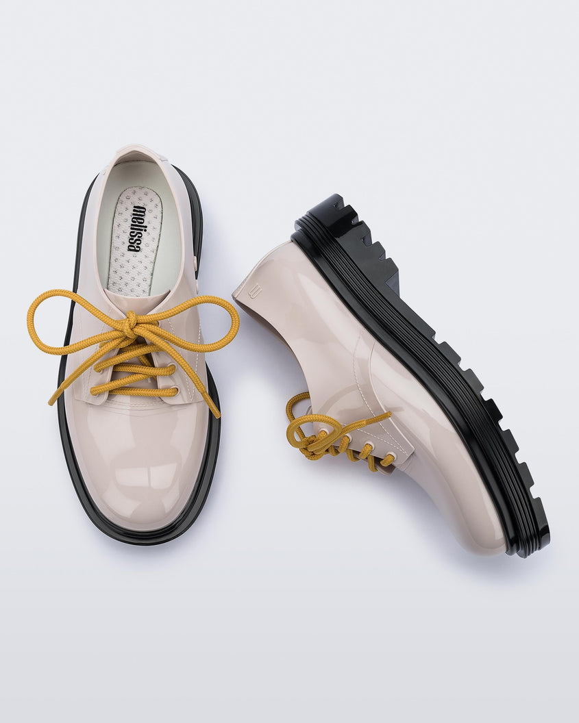 A side and top view of a pair of beige Melissa Bass sneakers with a beige base, yellow laces and a black sole.