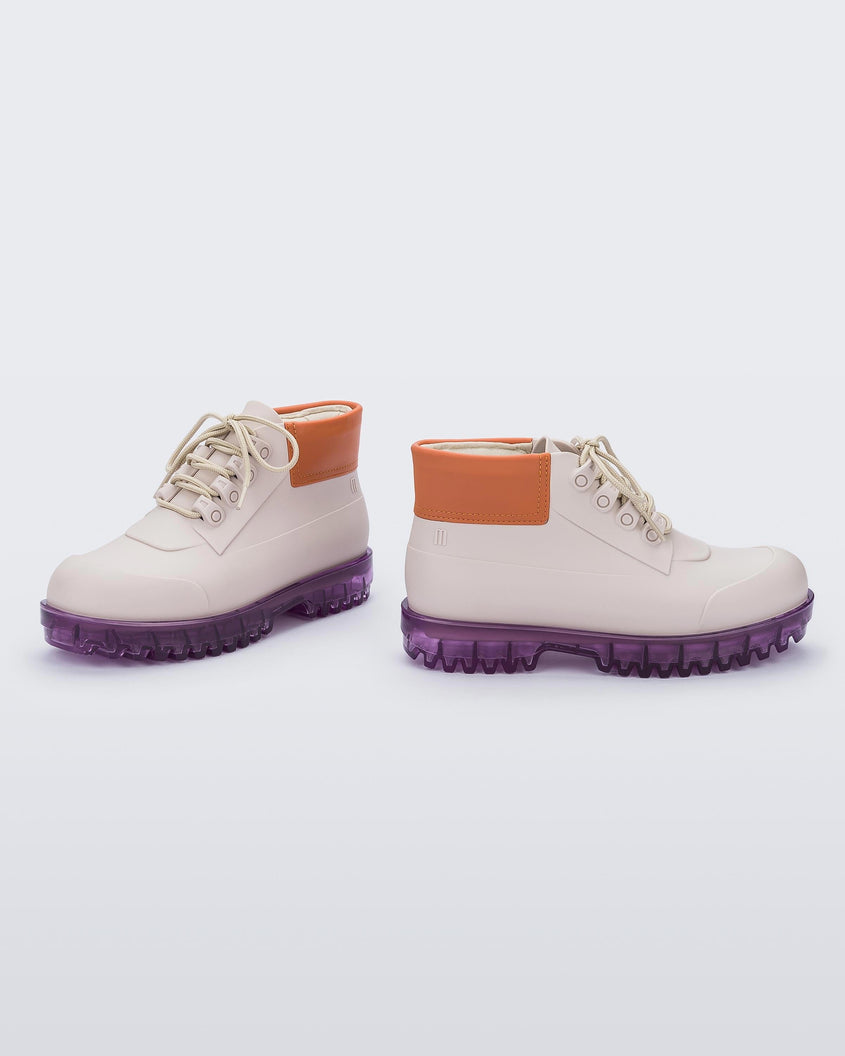 An angled inner and outter view of a pair of beige/orange/lilac Melissa Ares combat boots with a beige base, beige laces, orange top back and translucent lilac sole.