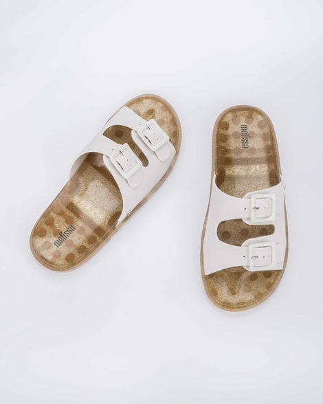 Top view of a pair of Melissa Wide slide sandals with gold glitter sole and white double straps with buckles