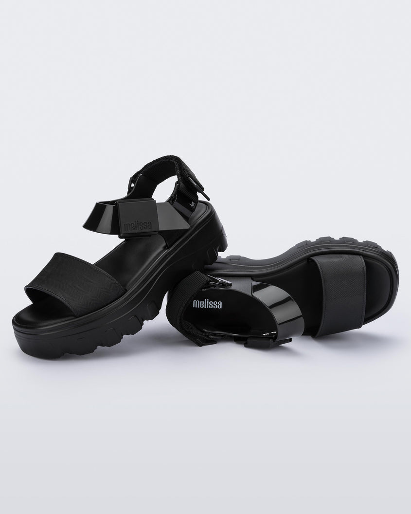 An angled top and side view of a pair of black platform Melissa Kick Off sandals with two straps.