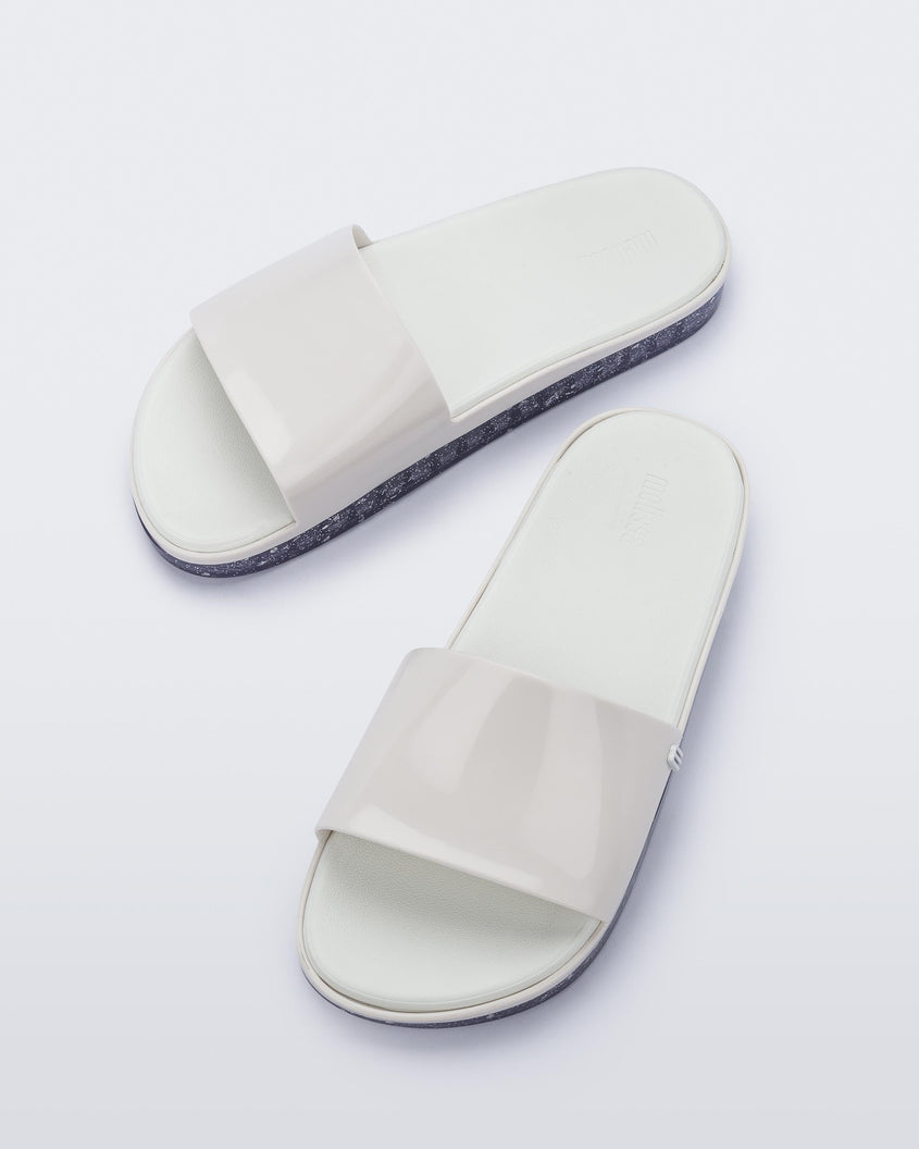 Angled view of a pair of white Melissa Beach slides with clear/glitter soles. 