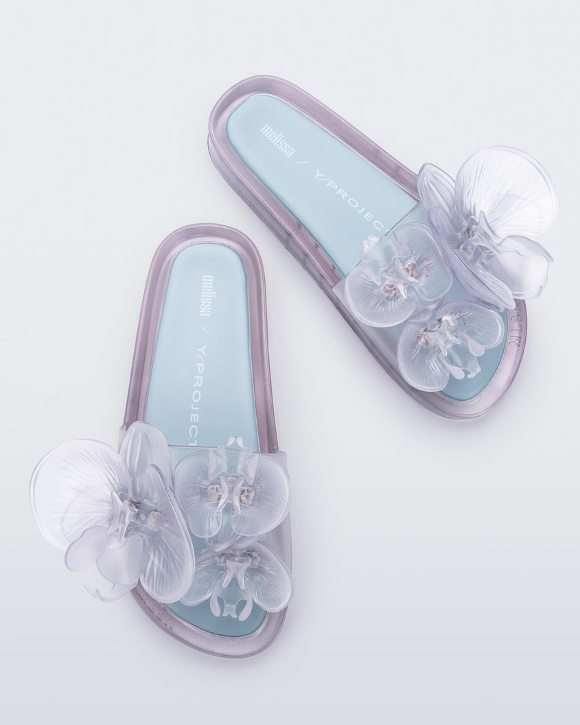 Top and angled view of a pair of Melissa Flower Beach slide in Clear with 3D flower on the strap and a light blue insole.