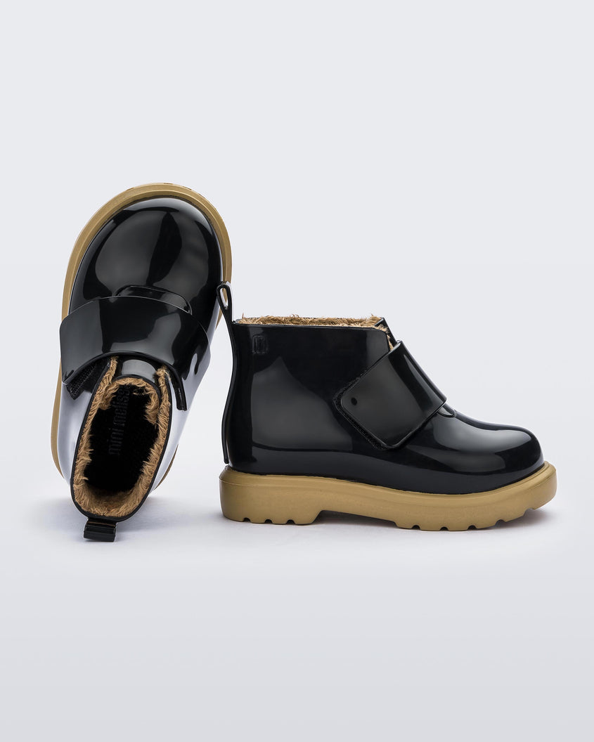 A top and side view of a pair of black/beige Mini Melissa Chelsea boots with a black base, velcro front strap and beige sole.