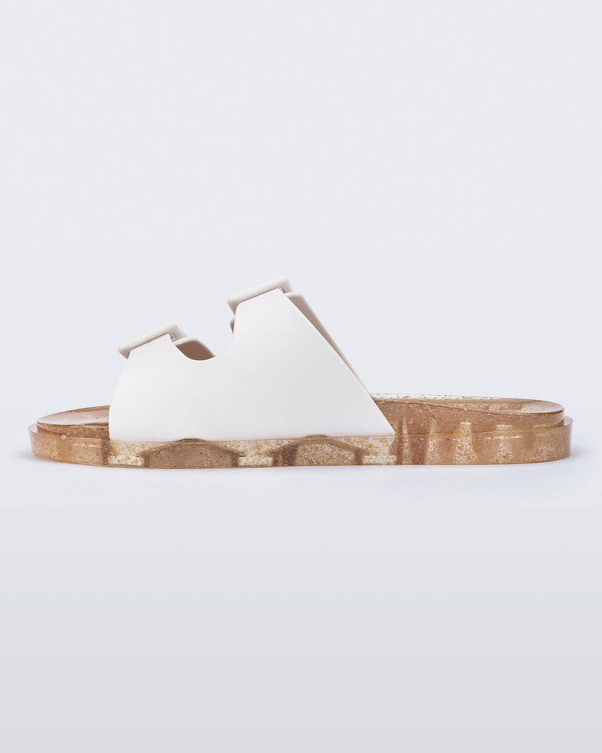Inner side view of a Melissa Wide slide sandal with gold glitter sole and white double straps with buckles