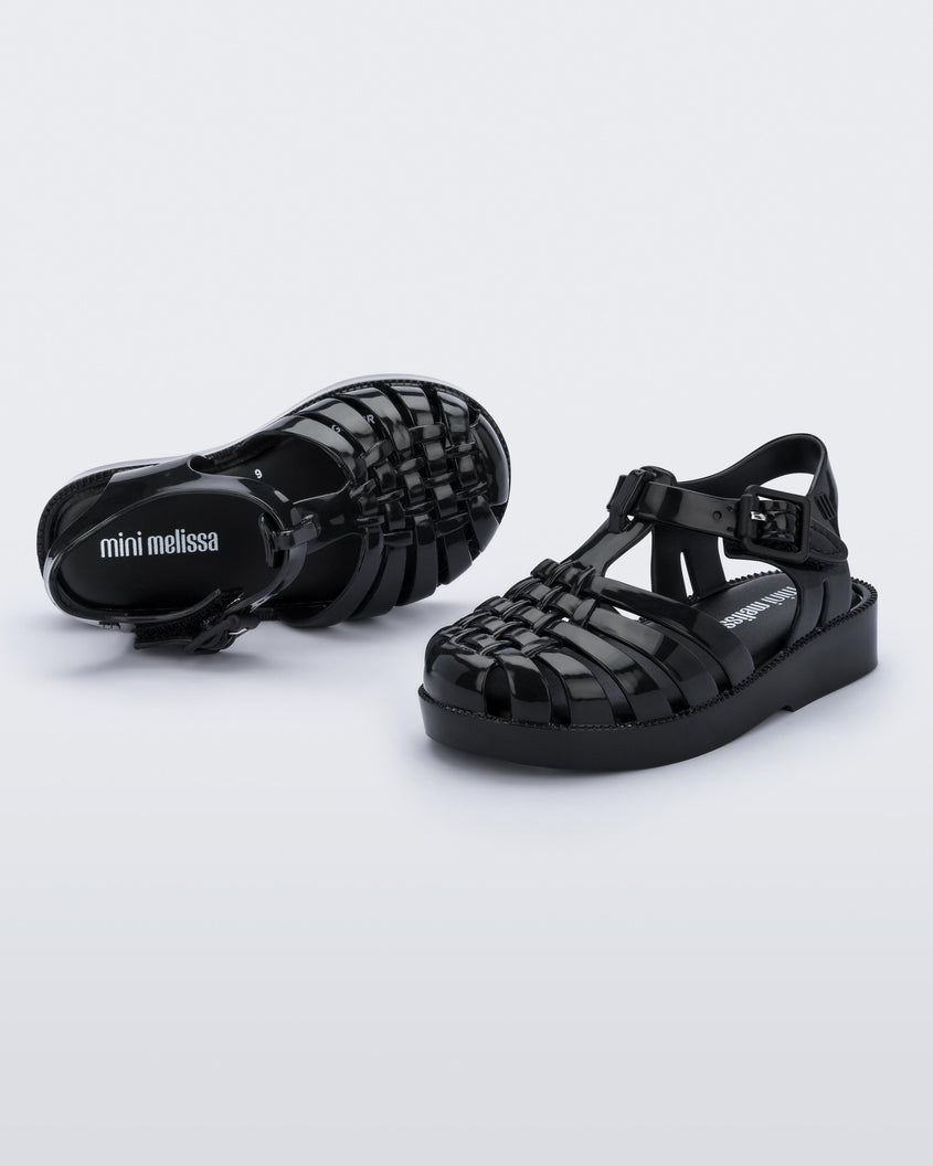 An angled front and top view of a pair of black Mini Melissa Possession sandals with several straps with a closed toe front.