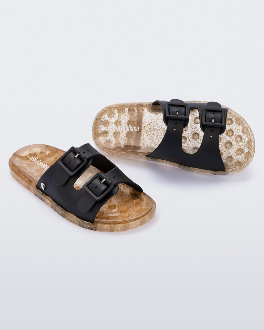 An angled front and top view of a pair of Black/Beige Mini Melissa Wide Slides with a black top with two black buckles and a beige sole.