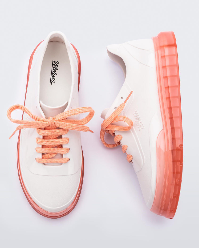 A top and side view of a pair of white Melissa Classic sneakers with a white base, laces, orange sole and a melissa logo on the side