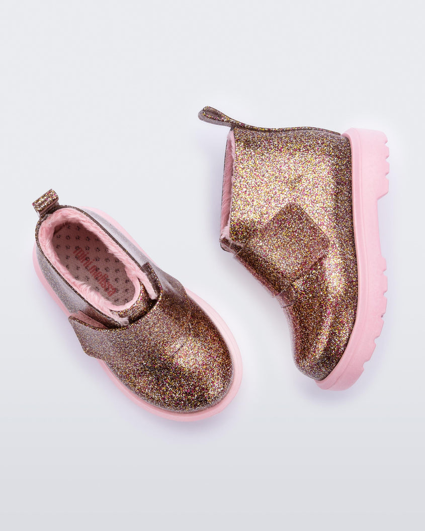 A top and side view of a pair of pink/glitter multicolor Mini Melissa Chelsea boots with a multicolor glitter base, velcro front strap and a pink sole.