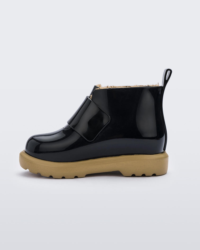 An inner side view of a black/beige Mini Melissa Chelsea boot with a black base, velcro front strap and beige sole.