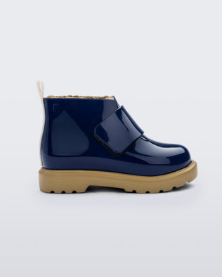 Side view of blue/beige Mini Melissa Chelsea blue boots with a velcro strap, dark blue base, beige sole and beige fuzzy lining.