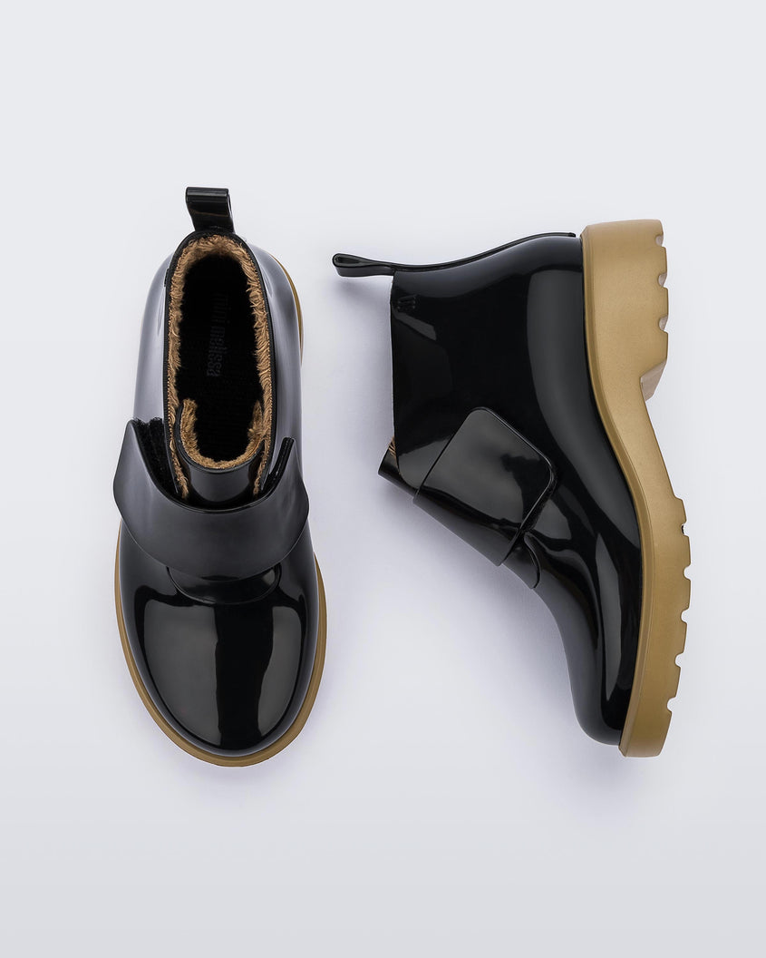 A top and side view of a pair of black/beige Mini Melissa Chelsea boots with a black base, black velcro front strap and beige sole.
