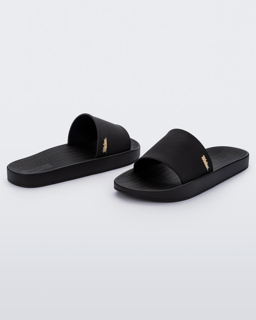 Back and front angled view of a pair of Melissa Sun Sunset slide sandals in black with gold Melissa logo on the top side corner of the strap. 