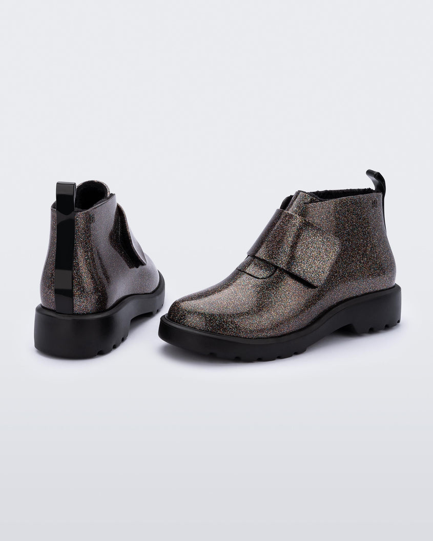 An angled side and back view of a pair of black/glitter multicolor Mini Melissa Chelsea boots with a glitter multicolor base, velcro front strap and black sole.