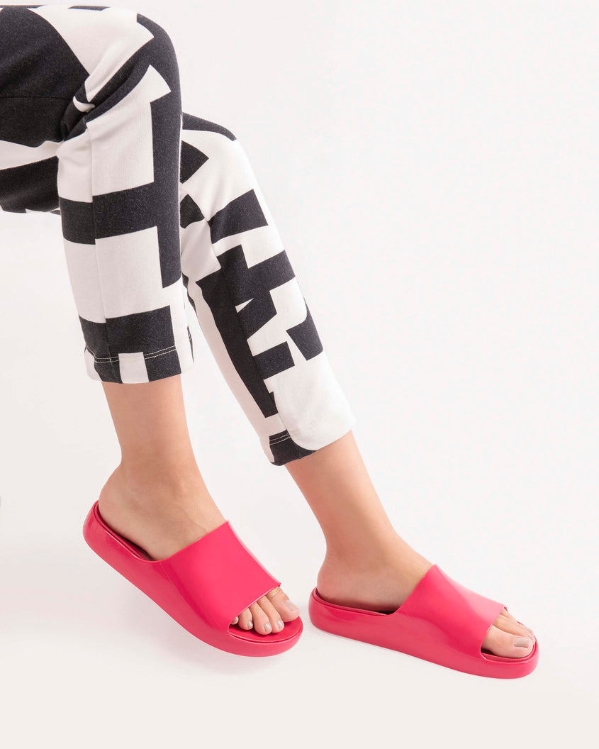 A model's legs wearing black and white pants and a pair of pink Melissa Cloud slides.