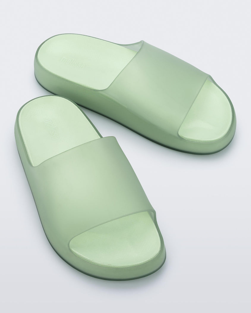 A top front view of a pair of transparent green Melissa Cloud slides.
